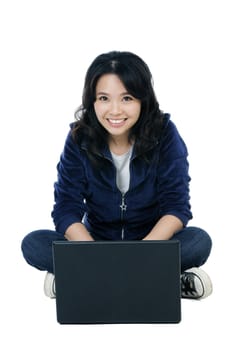 Portrait of a cheerful Asian woman sitting on floor using laptop over white background.