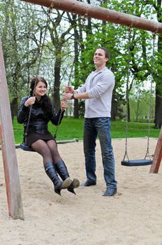 Guy rolls a girl on a swing in the park.