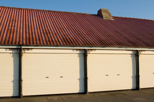 A Victorian pavillion building with red corrugated metal sheet roof, chimney, white shutters and metal structural posts against a blue sky.