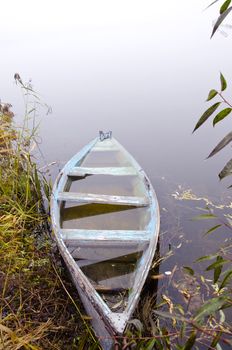 Sunken wooden boat filled with water stand on foggy river coast shore. Romantic transport.