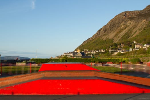 An outdoor skatepark with variuos ramps made from metal painted red with a cliff and blue sky in the background.