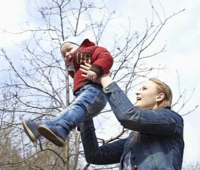 Happy young mother and her son laughing and playing together in the park. This shot was made in the first day of spring.