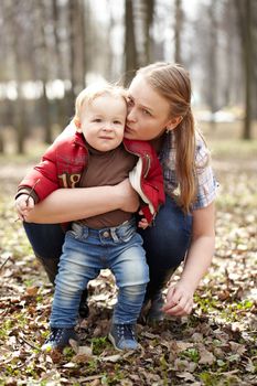 Beautiful young mother kissing and embracing her one year sonny in the park. This shot was made in the first day of spring.