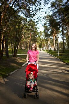 Young smiling mother with her 1 year son in the buggy walking outdoors in the park. Springday, natural colors, shallow dof (prime 35mm L optics)