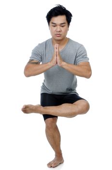 Portrait of a handsome Asian man doing yoga stance over white background.