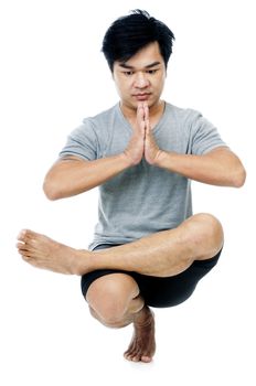 Portrait of a handsome young Asian man in yoga stance over white background.