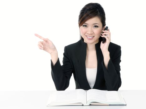 Portrait of an attractive young businesswoman talking on cellphone and pointing towards copypace, isolated on white background.