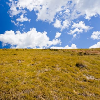 Hillside covered with dry yellow grass against blue sky with clouds