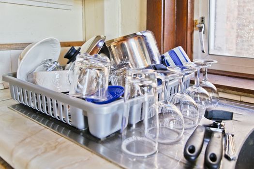 Sink in the corner of a UK cottage kitchen piled with washed up kitchen utensils