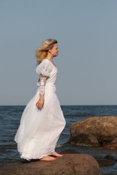 woman in white dress standing on a large stone at the beach