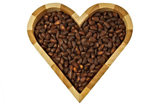 The wooden box in the shape of a heart with pine nuts inside, isolated on a white background, close-up.