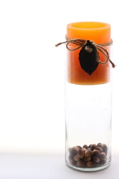 Orange candle in glass vase with acorns sitting on bottom.