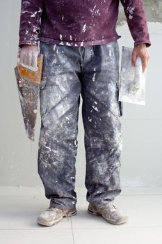 construction plastering man dirty trousers with trowel and saw in hand