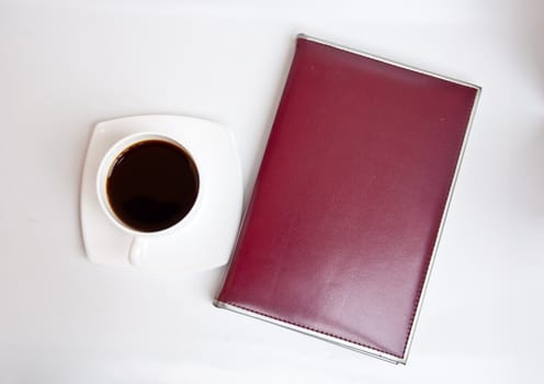 black coffee and brown notebook on white background