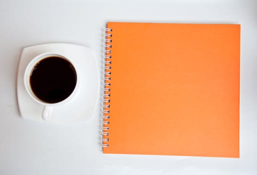 black coffee and orange notebook on white background