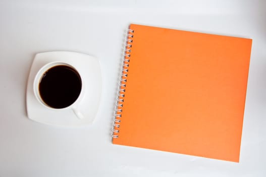 black coffee and orange notebook on white background