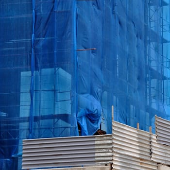 Building under debris netting at construction site. Aluminum fence and scaffold.