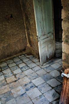 Abandoned house interior. Decayed room door with tiled floor and roots growing on crumbling brick wall.