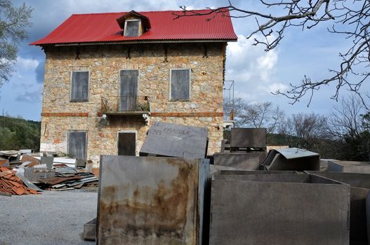 Derelict stone house with boarded windows pile of box crates and rubble.