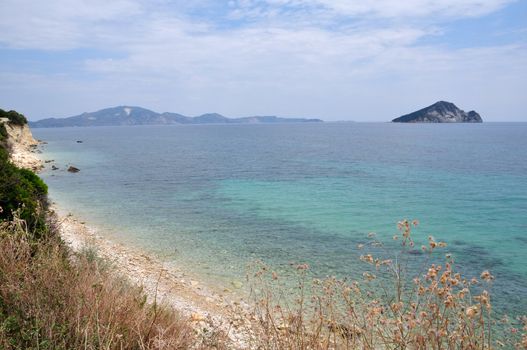 Empty eroded stone beach in Laganas bay Zakynthos, Greece. Distant view of Marathonisi islet natural caretta sea turtle habitat.