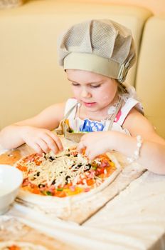 Little girl finally adding last ingredient - cheese - in pizza