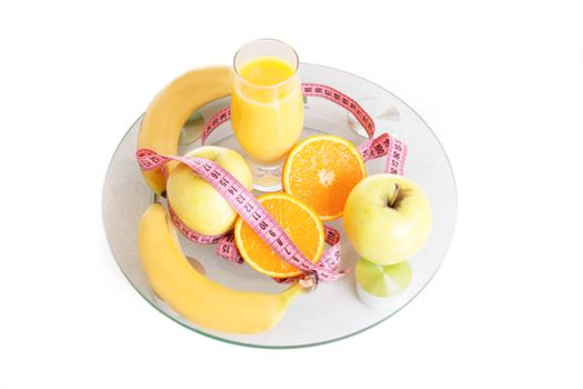 Some fruits, juice and measure tape on scales over white