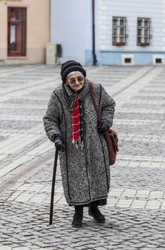 Image of a lonely senior woman walking in a paved city square.