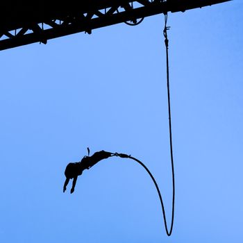Silhouette of bungee jumper against blue sky