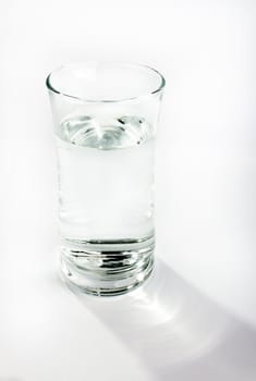 A single glass of water against a light gray background. Shadow commnig off the glass is visible