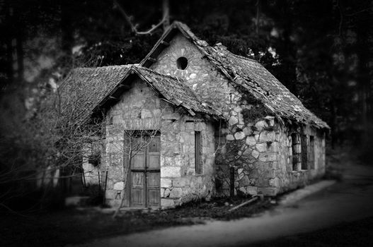 Derelict haunted stone house and dirt road in the woods. Black and white.