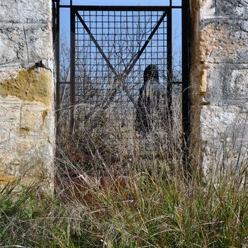 Man behind vintage metal door and overgrown grass in rural landscape.