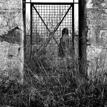 Man behind vintage metal door and overgrown plants in rural landscape.