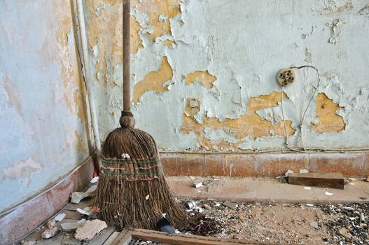 Dusty straw broom on filthy floor of abandoned house.
