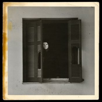 Vintage photograph of masked figure by the broken windows of abandoned house.