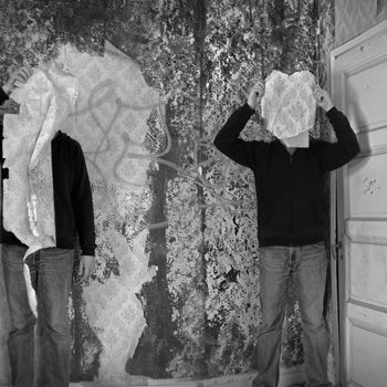 Two figures obscured by torn wallpaper shred in abandoned building interior.