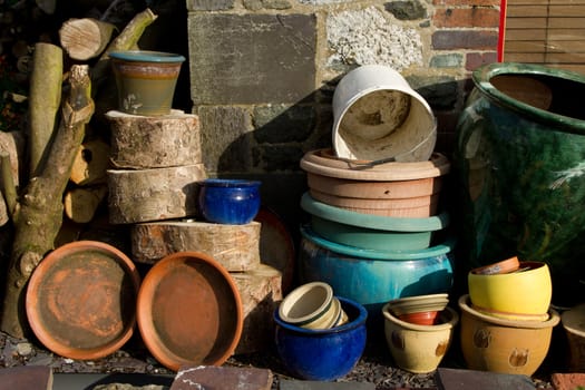 An assortment of plant pots of various shapes, colour and sizes stacked up in a garden amongst logs.