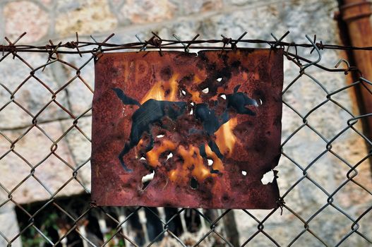 Rusty beware of the dog sign and chain link fence background.
