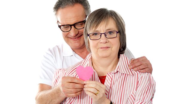 Portrait of smiling senior couple looking at camera with focus on paper heart