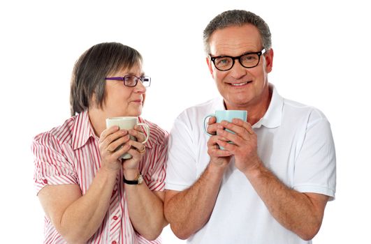 Romantic senior couple holding coffee mugs isolated over white
