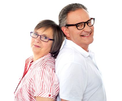Portrait of smiling aged couple posing back to back against white background