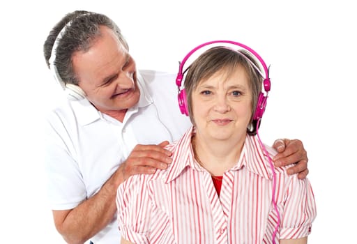 Aged couple enjoying music over white background. Man resting hands on shoulders of his wife