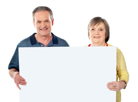 Smiling aged couple holding blank white poster showing it to camera