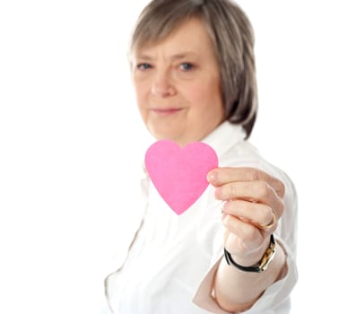Focus on pink paper heart. Aged woman holding it close to camera