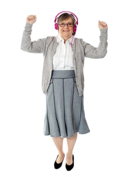 Cheerful aged woman enjoying music. Dancing with arms up
