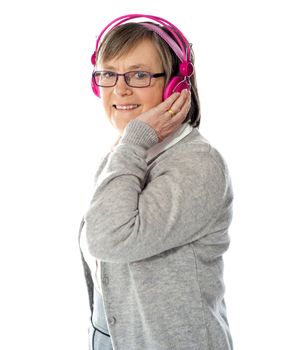 Aged woman holding earphones with one hand looking at you