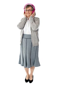 Aged lady listening music through pink headphones