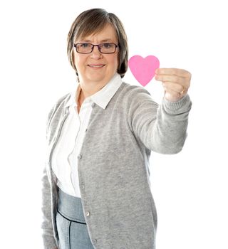 Female holding a pink paper heart, focus on the heart.
