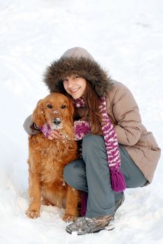 smiling teenager caucasian girl in hood hugging her dog outdoors at snow