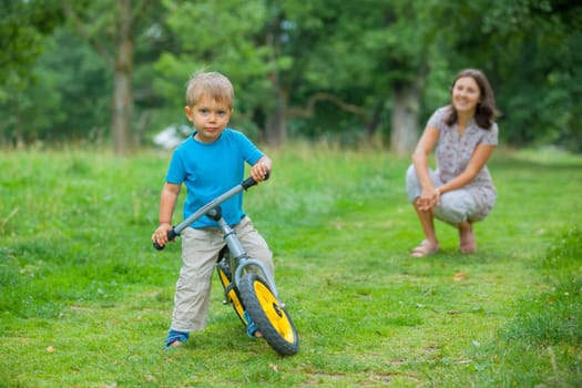 Portrait of little boy on a bicycle and his mother in the summer park