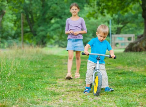 Portrait of little boy on a bicycle and his sister in the summer park